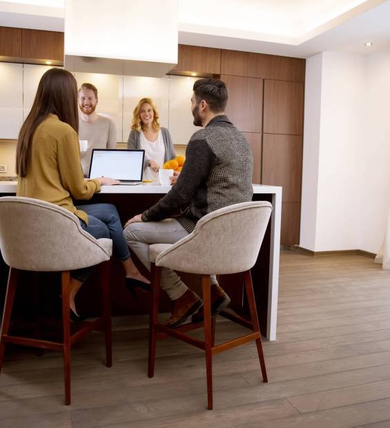 Group of happy young people preparing meal, looking for recipes on the laptop and having a good time