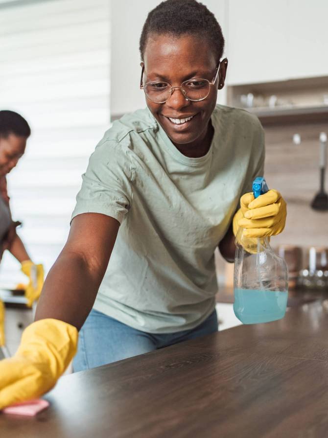 Two smiling african housekeepers wearing gloves and cleaning kitchen counter and floor